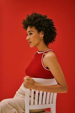 Genç bir kadın kendine güvenerek poz veriyor, cesur moda seçimini kırmızı zeminiyle kucaklıyor..