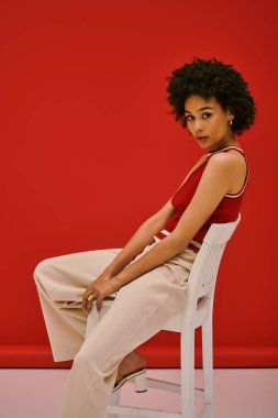 Şık genç bir kadın zarif bir şekilde bir sandalyede oturuyor, kendine güvenerek şık kıyafetiyle hava atıyor..