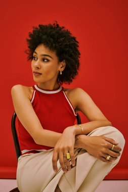 Genç bir kadın, şık bir kıyafete, koyu kırmızı bir arka plana karşı güven saçıyor..