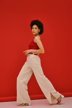 Şık bir genç kadın cesur bir kırmızı arka plana karşı özgüvenle poz veriyor..