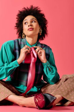 Zarif bir şekilde yerde oturan genç bir kadın, şık kravatını koyu pembe bir zemine göre ayarlıyor..