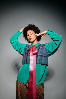 Tarz sahibi genç bir kadın, kareli kumaş ve geniş bir yay içeren canlı bir elbiseyle güven içinde poz veriyor..