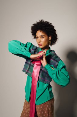 Genç bir kadın zarif pozlar veriyor, cesur kıyafetini ve kendine güvenen ifadesini bir stüdyoda sergiliyor..