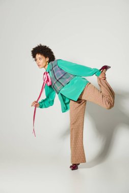 Canlı kıyafetli genç bir kadın neşeli bir poz veriyor, kendine güveni ve tarzı var..