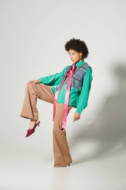 Kendine güveni tam genç bir kadın, modern bir stüdyoda canlı kıyafetini sergiliyor..