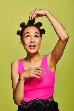 Parlak giyimli genç bir kadın, taze yeşil bir arka planda saçını şekillendirirken neşesini ifade ediyor..