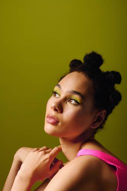 Cesur makyajlı ve eşsiz saç stili olan kendine güvenen genç bir kadın yeşil bir duvara karşı duruyor..