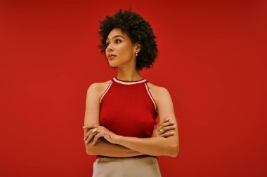 Genç, güzel bir kadın kendine güvenerek duruyor, kollarını şık bir kıyafetle kavuşturuyor..