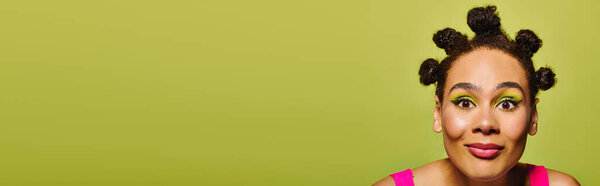 Charming woman showcases her creative hairstyle and colorful makeup against a lively backdrop.