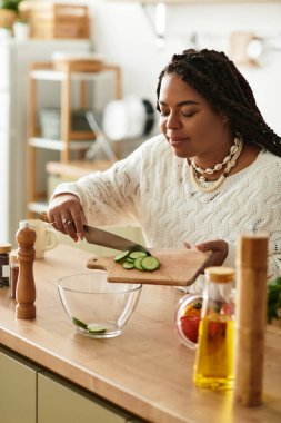 Sıcak bir mutfakta, genç bir Afrikalı Amerikalı kadın salata için dikkatlice salatalık doğruyor..