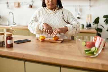 Genç bir Afrikalı Amerikalı kadın taze bir salata hazırlıyor, meyve ve sebzeleri dikkatlice dilimliyor..