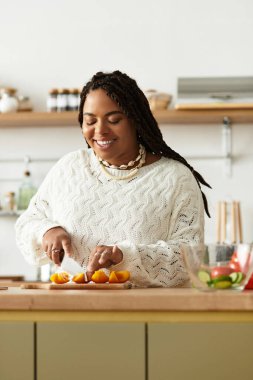 Genç bir Afrikalı Amerikalı kadın sıcak mutfağında canlı bir salata hazırlıyor, neşeyle gülümsüyor..