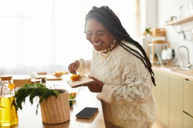 Genç bir Afrikalı Amerikalı kadın, rahat mutfağında renkli bir salata yapmaktan hoşlanıyor..