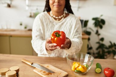 Genç siyah kadın rahat mutfağında renkli sebzeler sergilenen taze bir salata hazırlıyor..