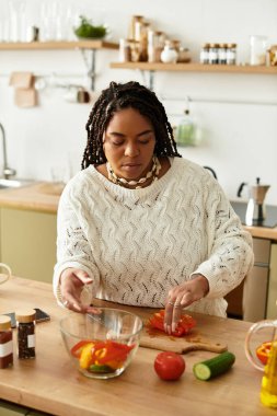 Genç siyah bir kadın mutfağında sağlıklı bir salata için taze sebze doğruyor..