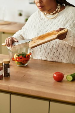 Genç siyahi bir kadın, evde canlı bir salata hazırlıyor ve aşçılığa olan sevgisini gösteriyor..