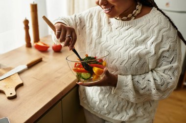 Genç bir Afro-Amerikan kadını evde canlı bir salata hazırlarken neşe odayı dolduruyor..
