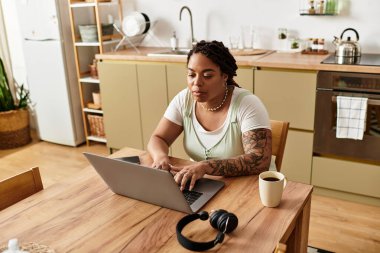 Kararlı genç bir Afrikalı Amerikalı kadın kahvesini içerken dizüstü bilgisayarında yazıyor..