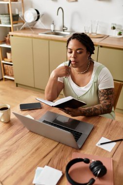 Odaklanmış genç bir kadın rahat masasında not alırken dizüstü bilgisayarıyla çalışıyor..