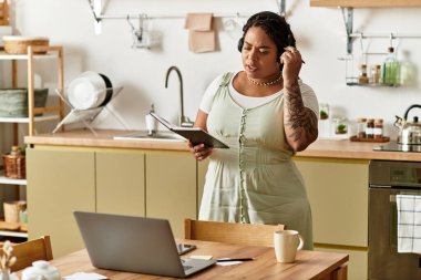 Kulaklık takıyor, evde tablet tutarken dizüstü bilgisayarıyla çalışıyor..