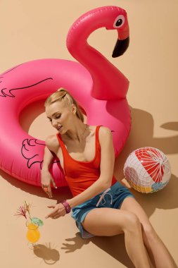 Genç bir kadın güneşli bir günde canlı pembe flamingo şamandırasının yanında içmekten zevk alır..