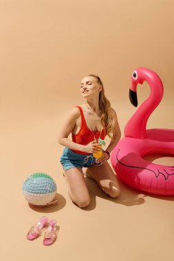 Genç bir kadın bir kokteyl ve renkli bir flamingo ile güneşin altında poz veriyor..