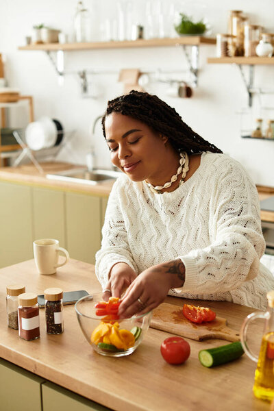 Молодая афроамериканка с радостью готовит красочный салат на своей стильной кухне.