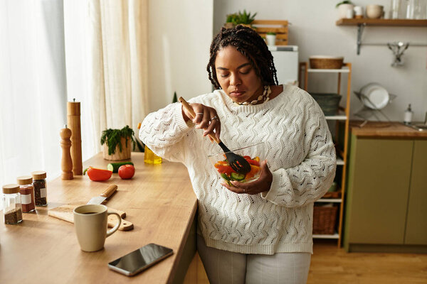 A young african american woman stirs a colorful salad with care in a bright kitchen.