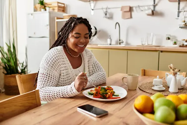 Genç bir kadın öğle yemeği saatinde rahat mutfağında renkli bir salatanın tadını çıkarıyor..