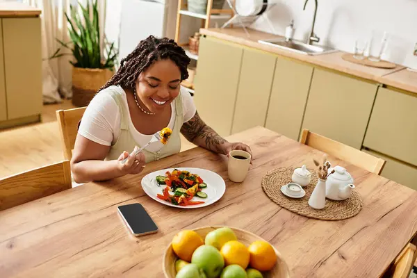 Genç bir Afrikalı Amerikalı kadın evde yemeğinin tadını çıkarırken taze salatadan zevk alıyor..