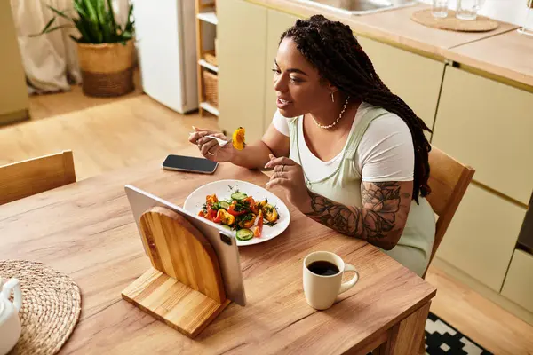 Genç bir Afrikalı Amerikalı kadın öğle yemeği sırasında evde salata yiyor ve her lokmanın tadını özenle çıkarıyor..