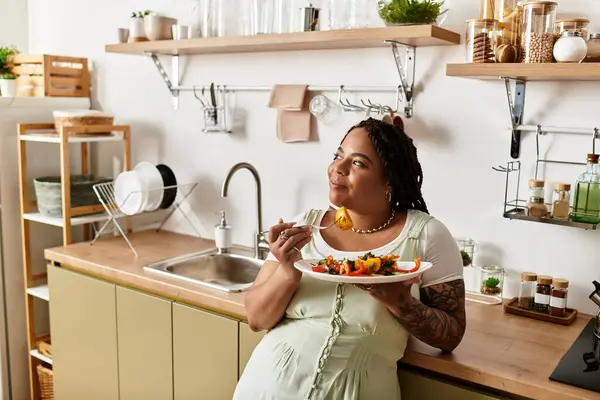 Sıcak bir mutfakta, genç bir Afrikalı Amerikalı kadın neşeyle taze salatanın tadını çıkarıyor..