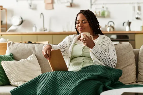 Genç bir kadın evde rahat rahat otururken sıcak bir içki ve kitapla sakin bir sabahın tadını çıkarıyor..