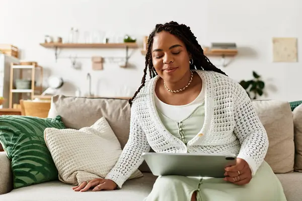 Rahat bir kanepede oturan genç bir kadın, tabletiyle huzurlu bir sabahın tadını çıkarıyor..