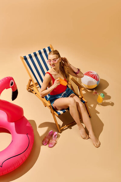 A young beautiful woman lounges on a stripy chair, sipping a drink under the warm sun at the beach.