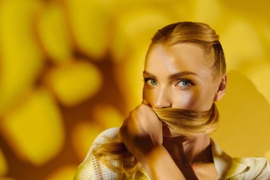 Mavi gözlü genç bir kadın saçlarıyla poz veriyor, etrafında sıcak sarı renkler var..