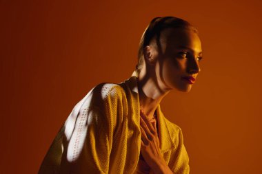 Genç ve güzel bir kadın, alacakaranlıkta sıcak turuncu bir zemine çarpıcı bir moda sergiliyor..