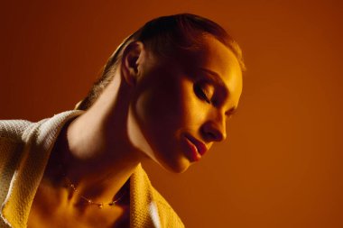 Güzel genç bir kadın, yumuşak bir ortamda sıcak tonlarla aydınlatılan zarafetini sergiliyor..