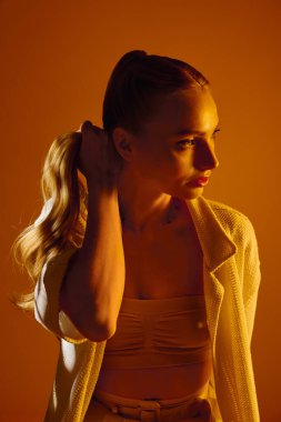 Saçları taranmış genç bir kadın zarif bir şekilde ışık altında poz veriyor, kendinden emin..