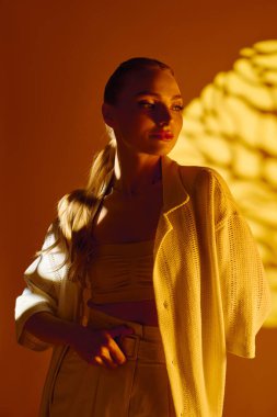 Genç bir kadın sıcak altın tonlarda zarif duruyor, modern moda eğilimlerini somutlaştırıyor..
