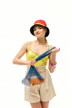 Modayı takip eden genç bir kadın poz verirken renkli meyve torbasını gösteriyor..