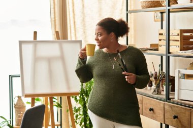 Yetenekli bir kadın sanat malzemeleri ve ilham kaynağıyla dolu rahat bir atölyede çayının tadını çıkarır..