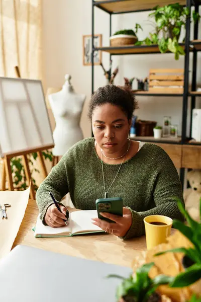 Güzel bir kadın canlı bir atölyede telefonunu kullanırken defterine odaklanır..