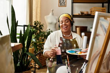 Neşeli bir kadın yeşilliklerle dolu güneşli bir atölyede resim yapıyor..