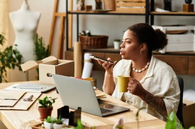 Güzel bir kadın, bir zanaat atölyesinde oturuyor, elinde bir bardak tutarken dikkatle çalışıyor..