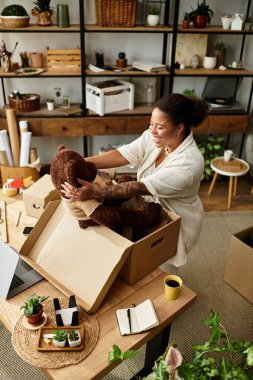 Güzel bir kadın büyük bir oyuncak ayıyı neşeyle dolu atölyesine yerleştirirken gülümsüyor..