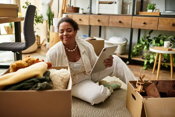 Bir zanaat projesiyle meşgul olan bir kadın, etrafı organize malzeme ve kutularla çevriliyken gülümsüyor..