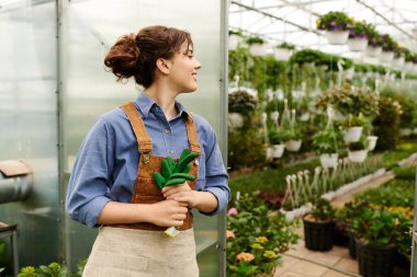 Parlak bir serada, genç bir kadın büyüyen bitkilerini sevgiyle besliyor, neşe saçıyor..