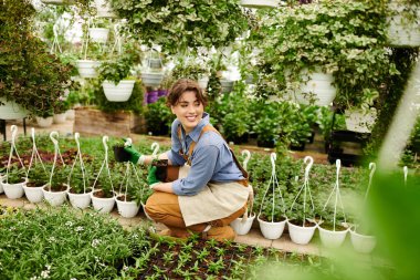 Genç bir kadın yeşillik dolu parlak bir serada gelişen bitkileriyle ilgilenir..