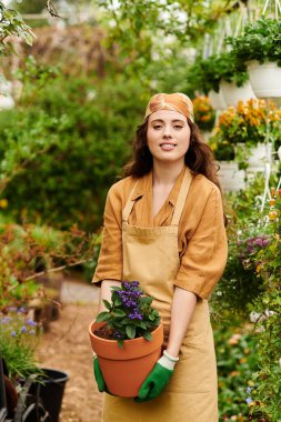 Huzurlu bir serada, genç bir kadın başörtüsü takarken canlı bitkileriyle ilgilenir..